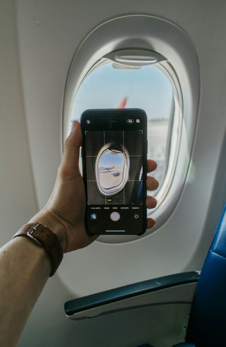 A hand holding a phone up to an airplane window